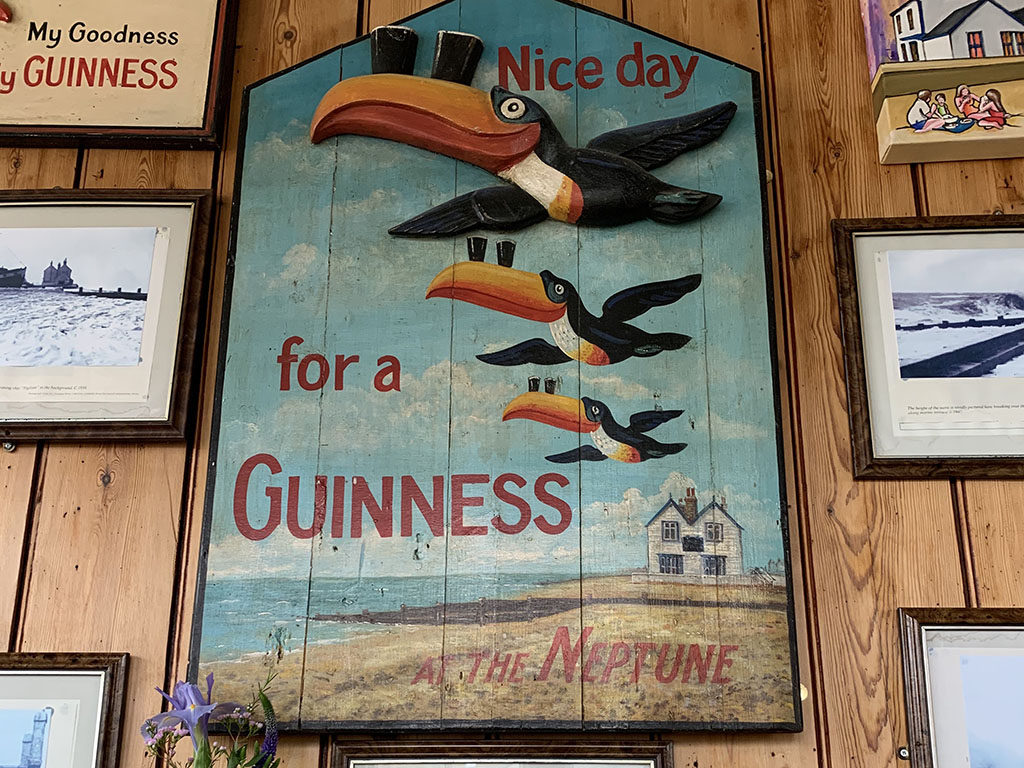 Photo of an old fashioned Guinness advert with three toucans flying over a small white wooden pub on a beach with text saying "Nice day for a Guinness at the Neptune"