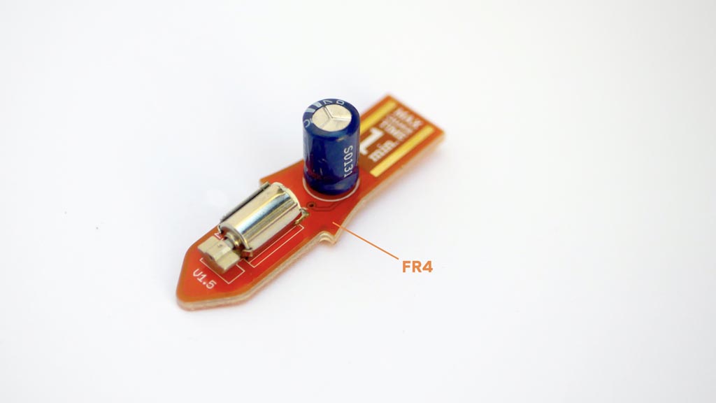 Photo of a small circuit board with a capacitor and motor on it. The circuit board itself is labelled "FR4"