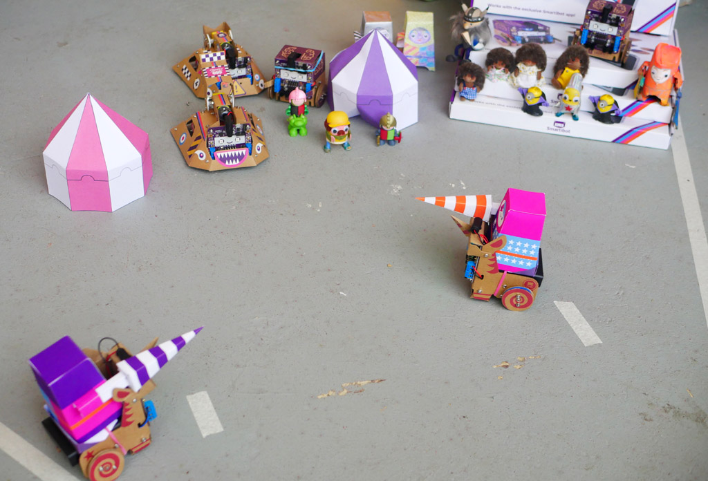 Photo of two brightly coloured paper knights riding cardboard robot unicorns. In the background small toy figures are cardboard robots look on